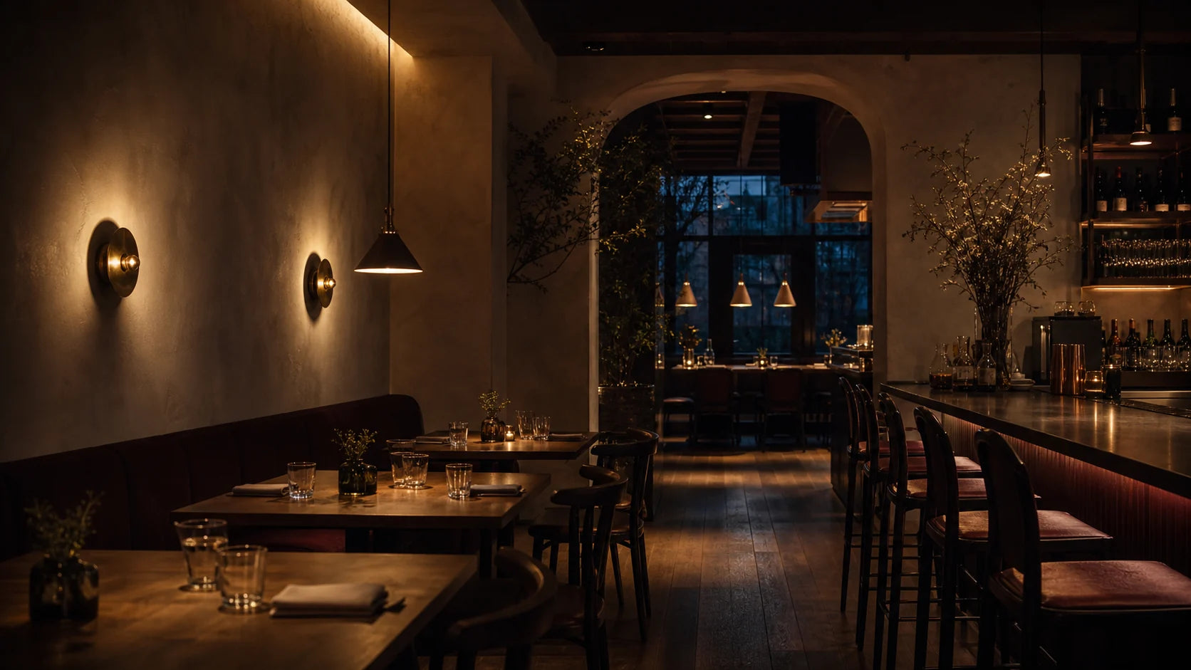 Layered restaurant lighting with warm pendants, wall sconces, bar lighting, and a softly lit circulation path